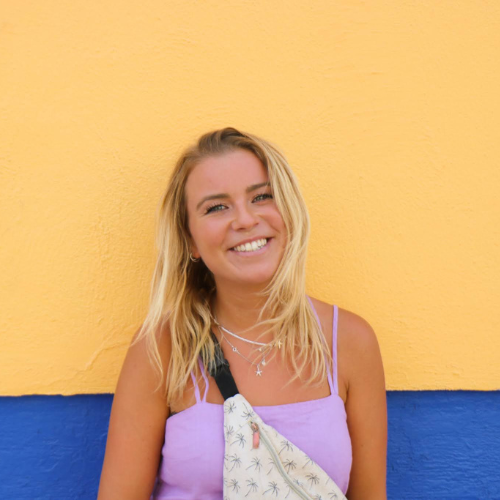 Uitgelichte foto medewerker, Eva, voor een gele muur met een blauwe onderkant