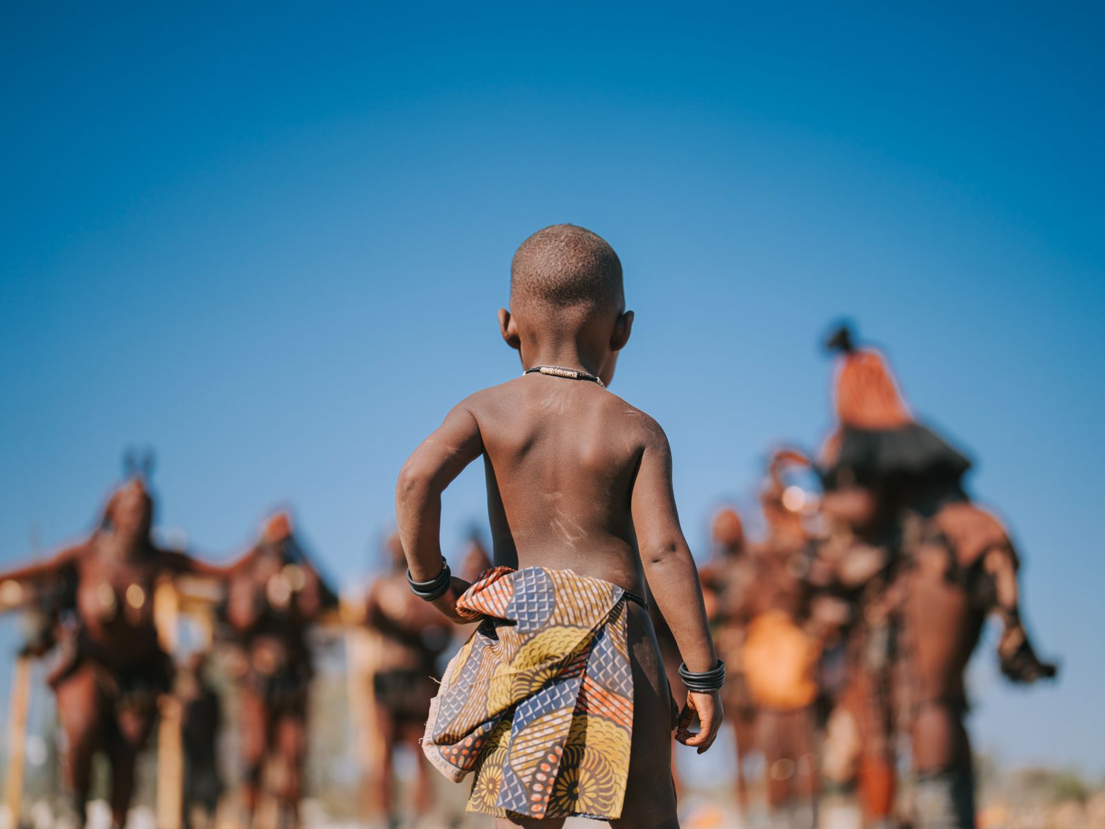 Rondreis Namibië, Kaokoland, Himba-bevolking kind met mensen op achtergrond