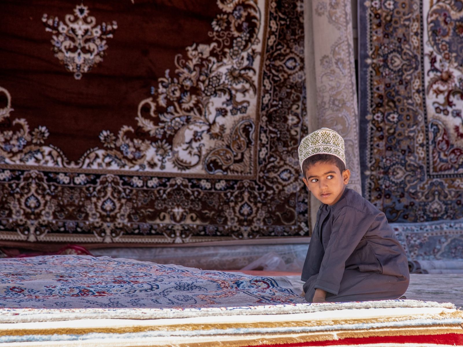 Rondreis Oman, Ibra, jongen op tapijten