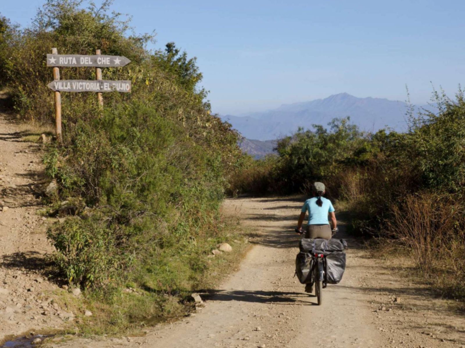 Rondreis Bolivia, Samaipata, excursie 4WD in de voetsporen van Che, vrouw op de motor op de weg met blauwe lucht en wegwijzer
