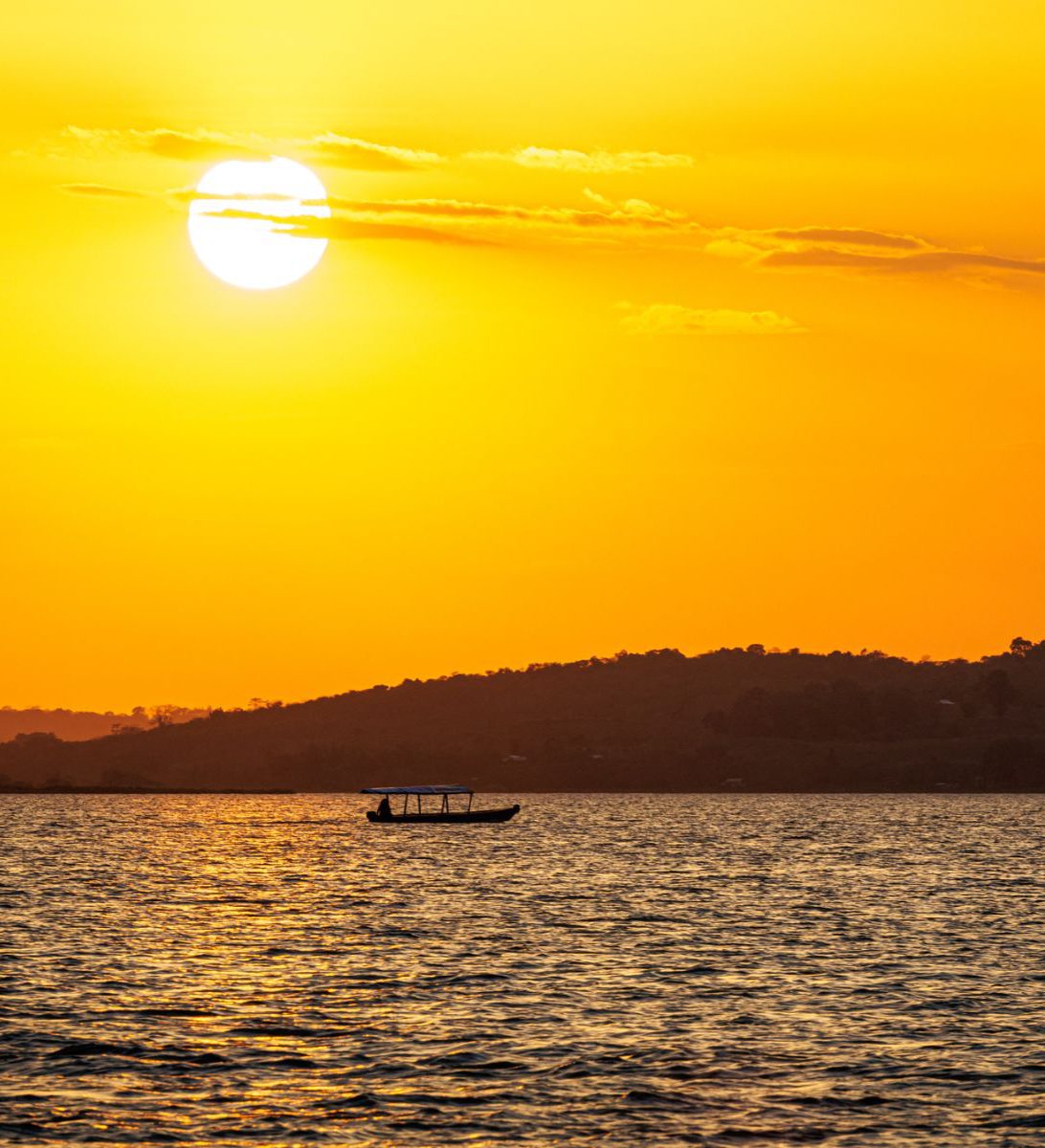 Rondreis Guatemala, Flores, excursie kajakken bij zonsopkomst op het Petén meer, zonsopkomst met bootje op achtergrond