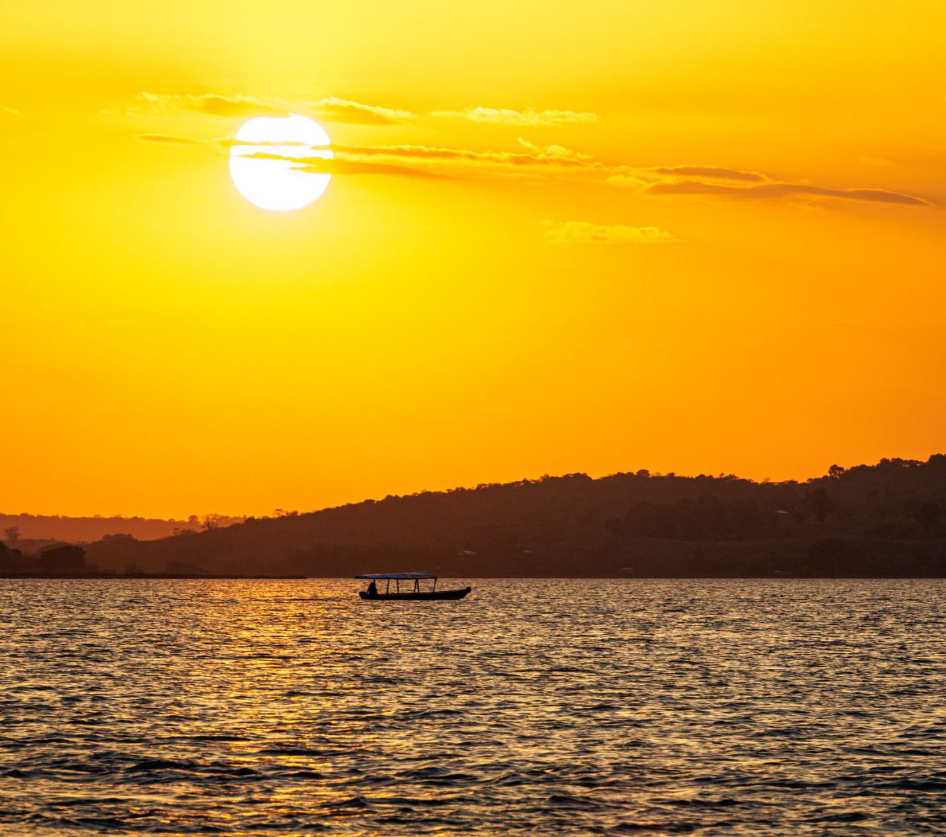 Rondreis Guatemala, Flores, excursie kajakken bij zonsopkomst op het Petén meer, zonsopkomst met bootje op achtergrond