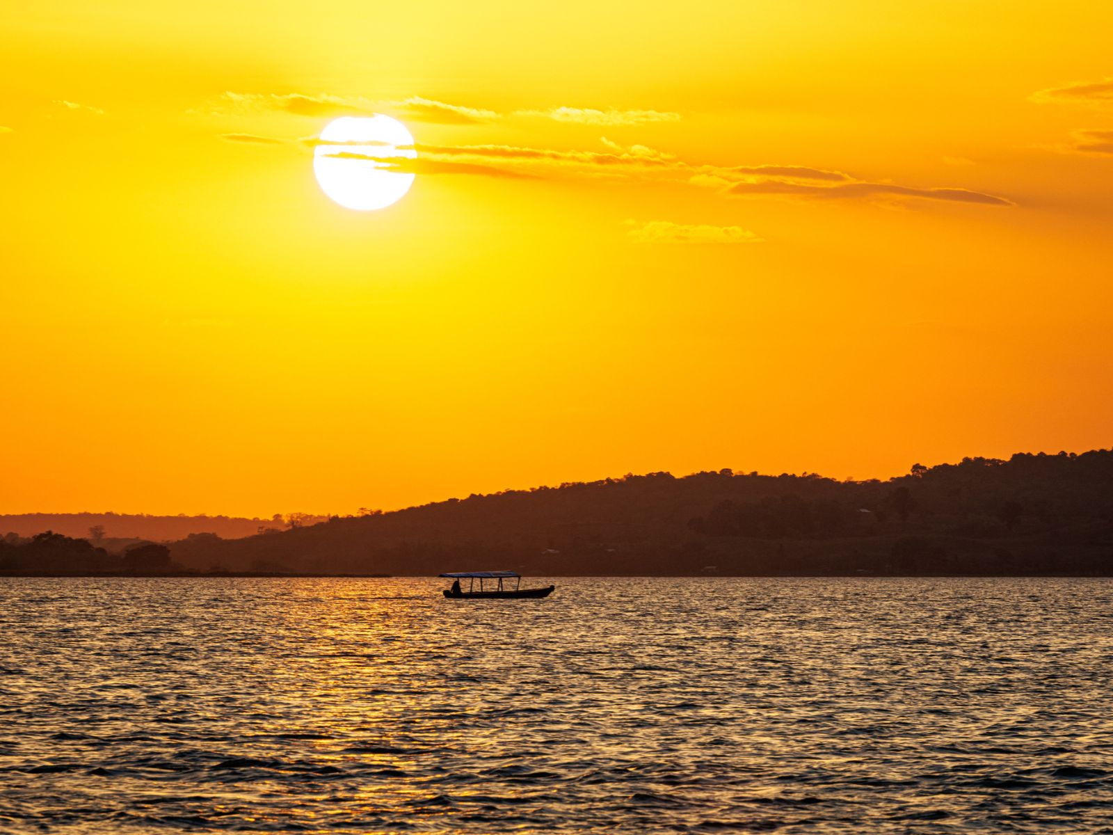 Rondreis Guatemala, Flores, excursie kajakken bij zonsopkomst op het Petén meer, zonsopkomst met bootje op achtergrond