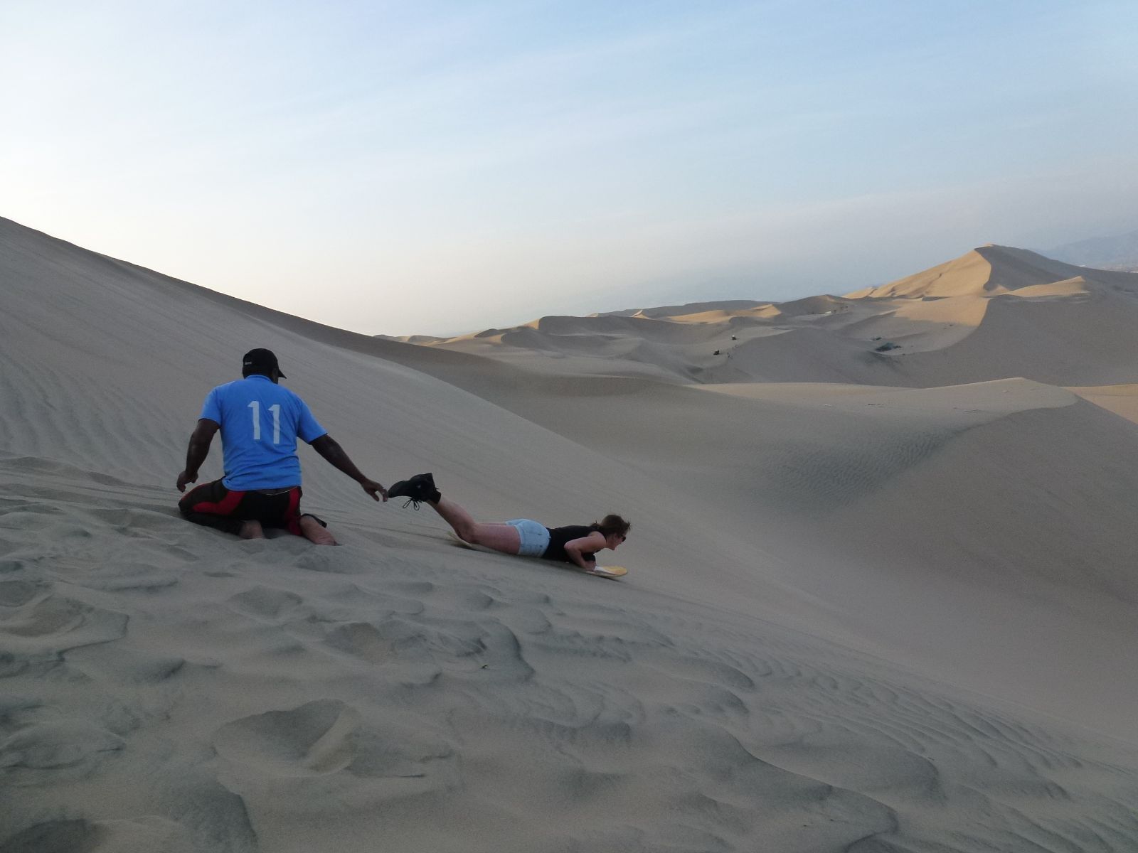 Rondreis Peru, Ica, excursie sandboarden en buggyrijden in Huacachina, persoon sandboarden op zandduin